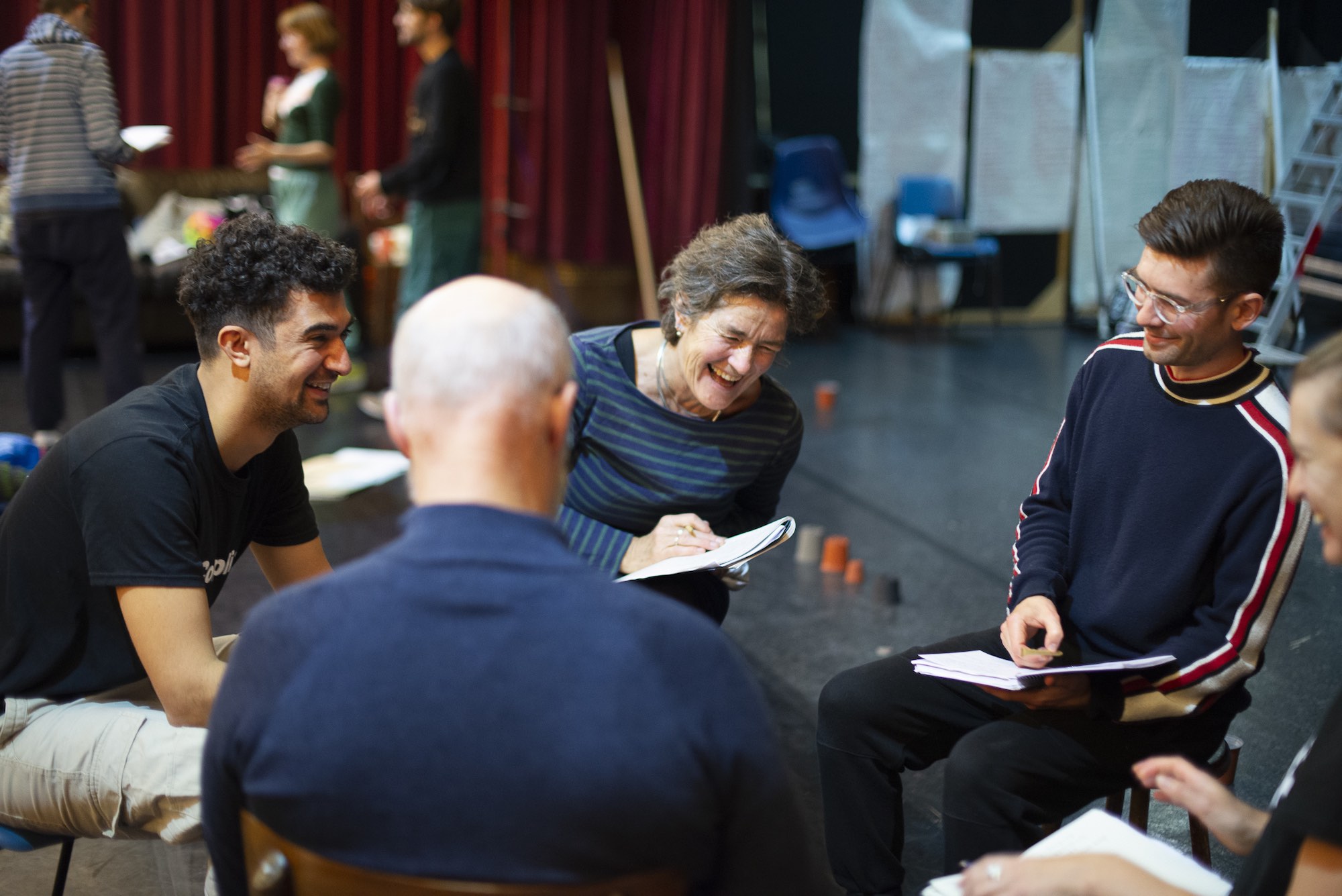 The actors sit in a circle and laugh together as they discuss ideas and write them in their notebooks