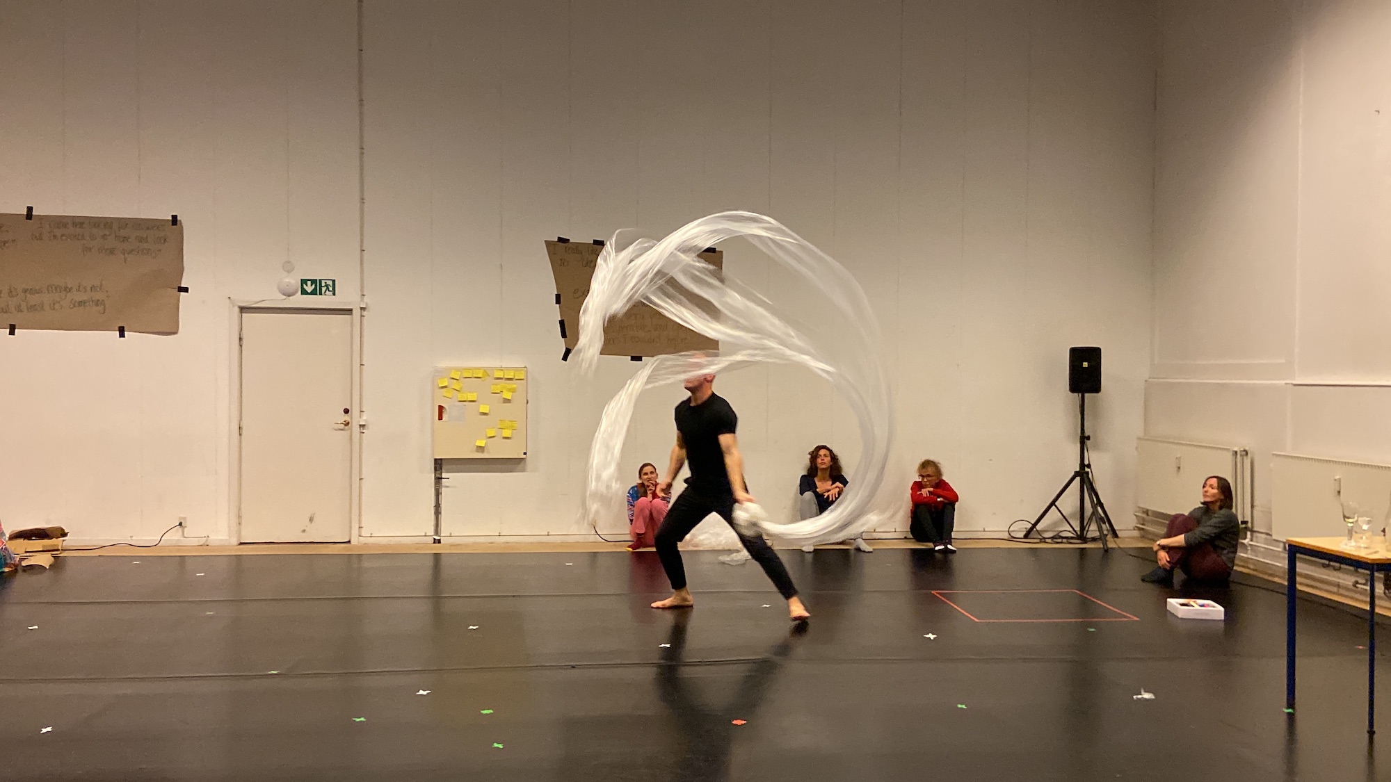 A participant wearing black moves with a long piece of white material, whirling it poetically around their body.