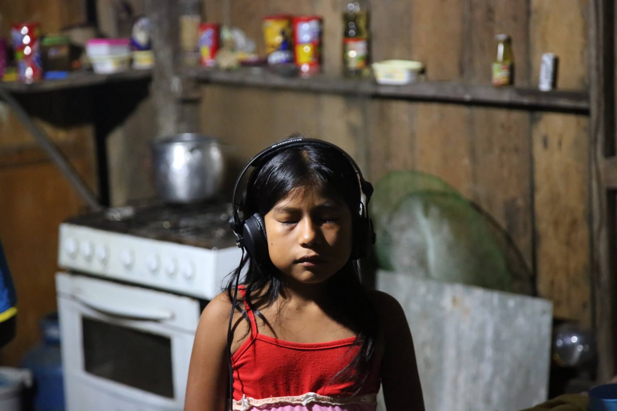 A child in a kitchen closes their eyes and listens to audio through a set of headphones