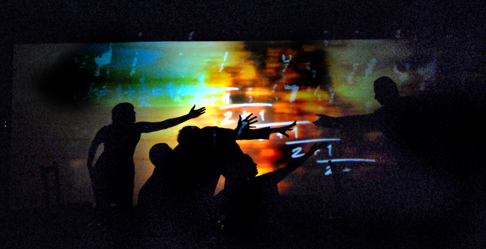 A group of shadowy actors reach towards a shadowy figure on their right, who is also reaching towards them, while we see mathematical theorems projected on the back stage in fire colours