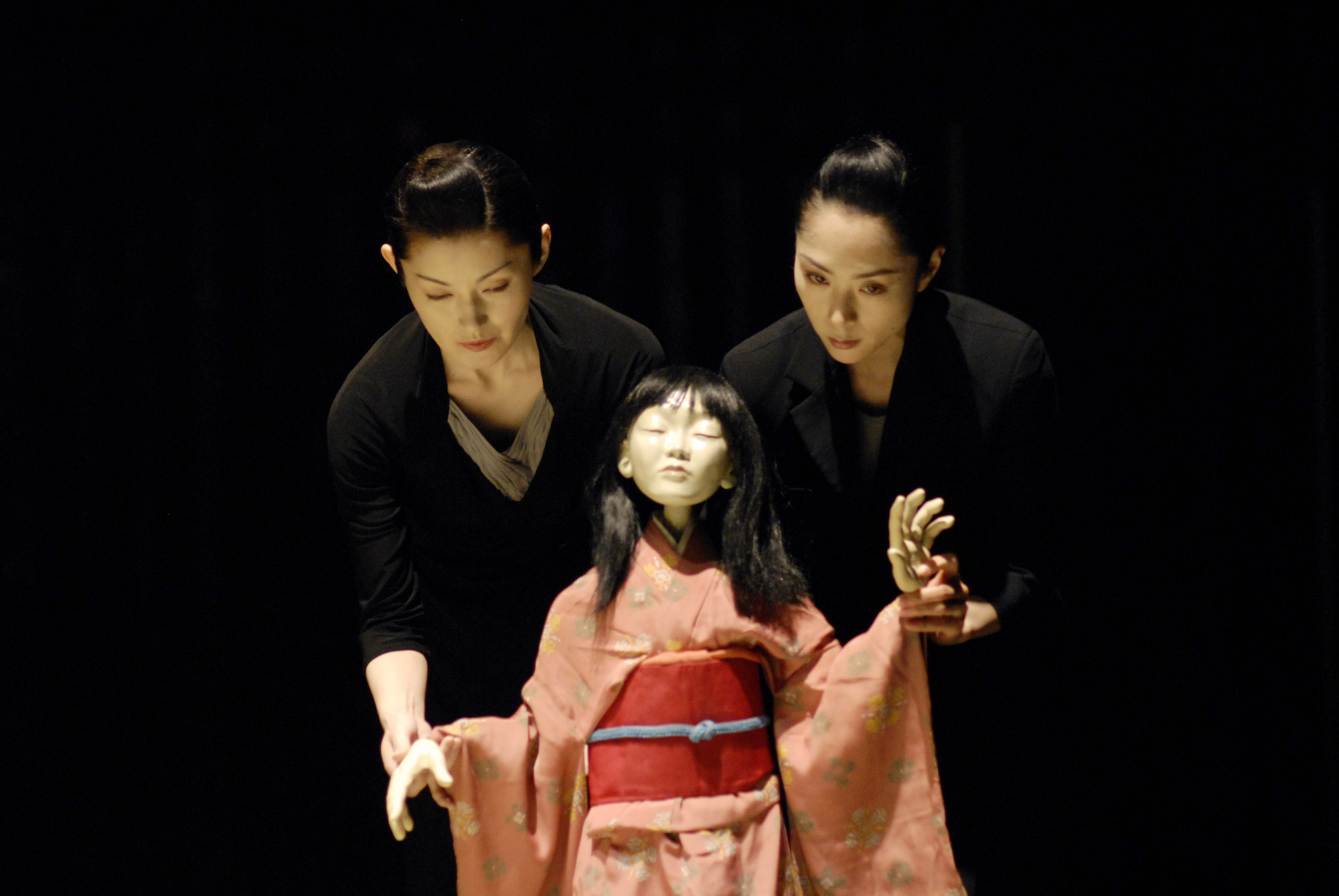 A puppet woman wearing a pink kimono steps forward assertively