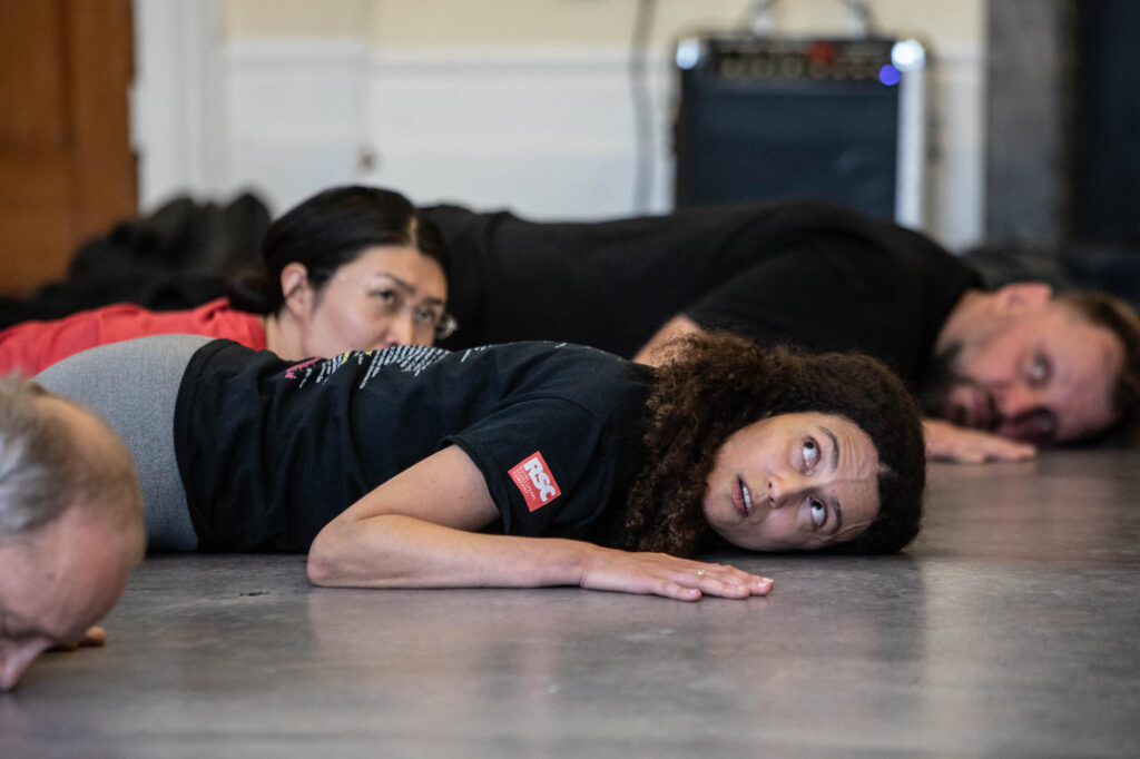 Four workshop participants lie on the floor, looking wary.