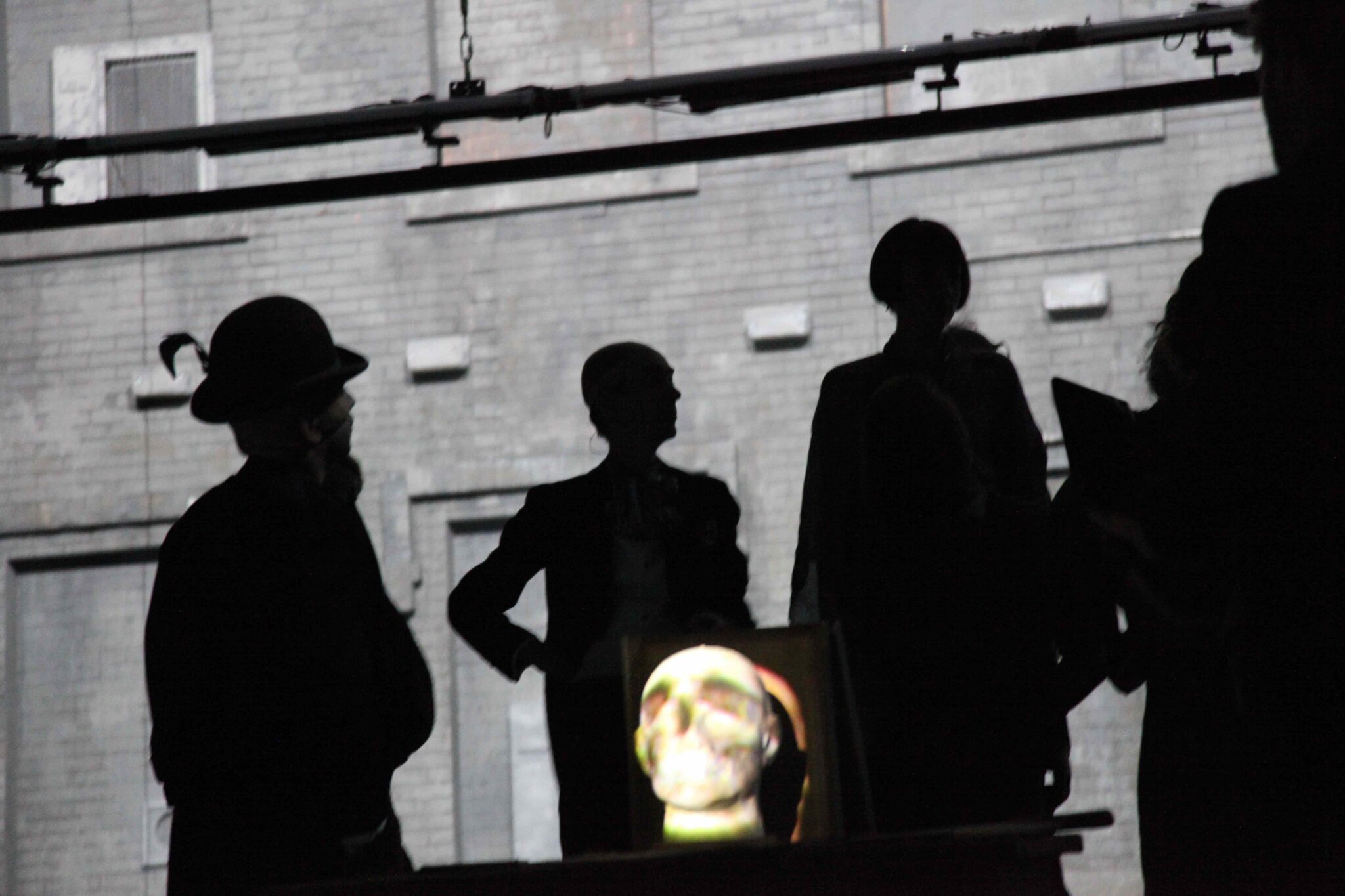 Four shadowy figures in the background and a skull is seen in the foreground