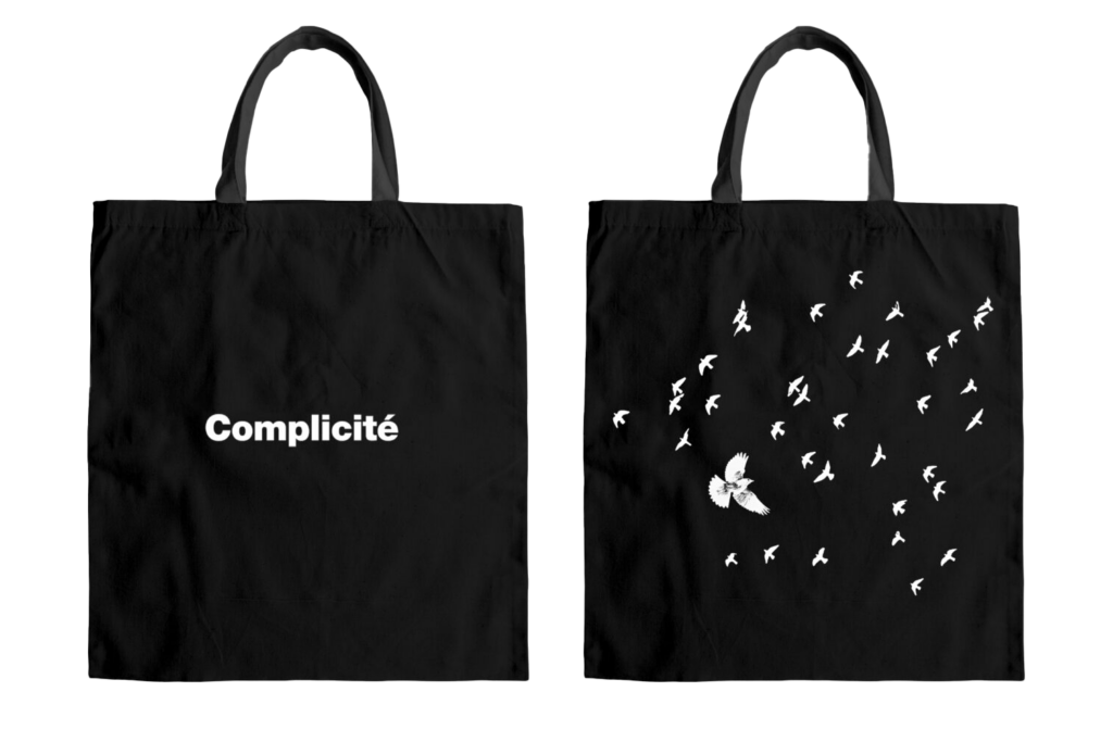 The front of this black tote bag reads Complicité in white letters, while the back of the bag shows one large bird flying surrounded by lots of little birds, all in white.